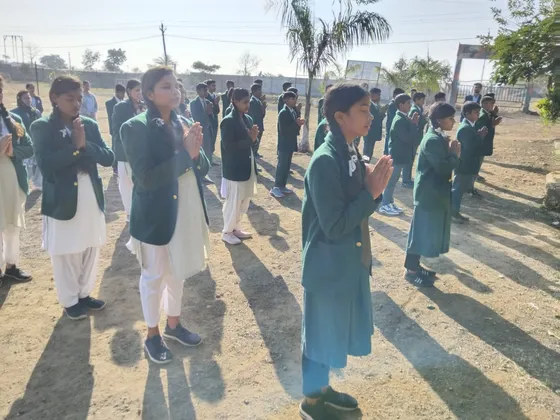 Girls in green school blazers stand with folded hands during morning prayer.