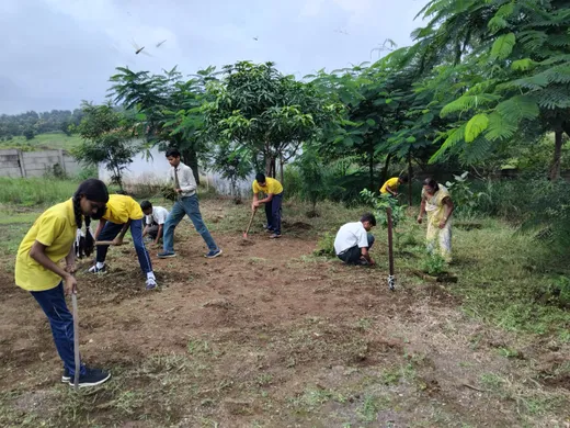 Students and a teacher dig and plant saplings on campus during the monsoon.