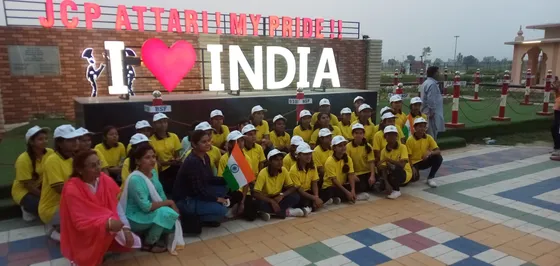 Students in white caps and yellow T-shirts sit in front of an 'I love India' sign at the Attari border.