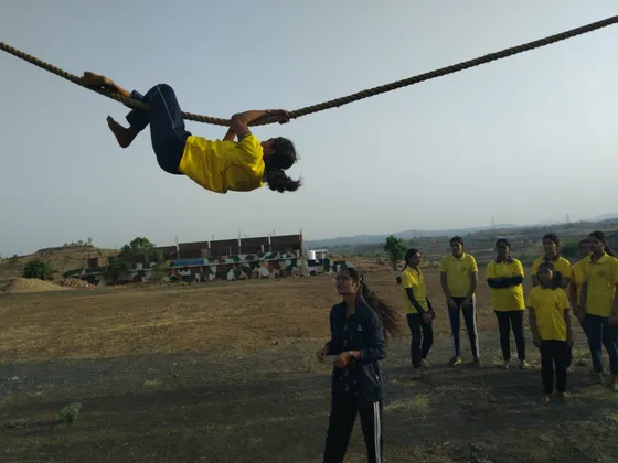 A student in the yellow Ojas T-shirt crosses a rope obstacle while her classmates and instructor watch.